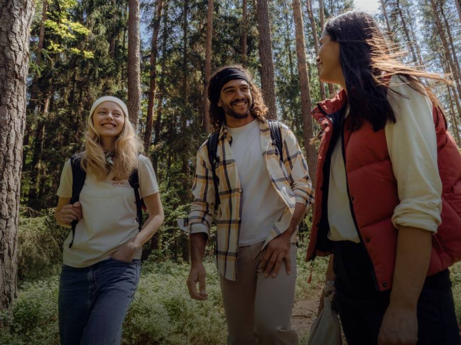 Drei lächelnde Wanderer in lässiger herbstlicher Wanderkleidung im sonnigen Wald