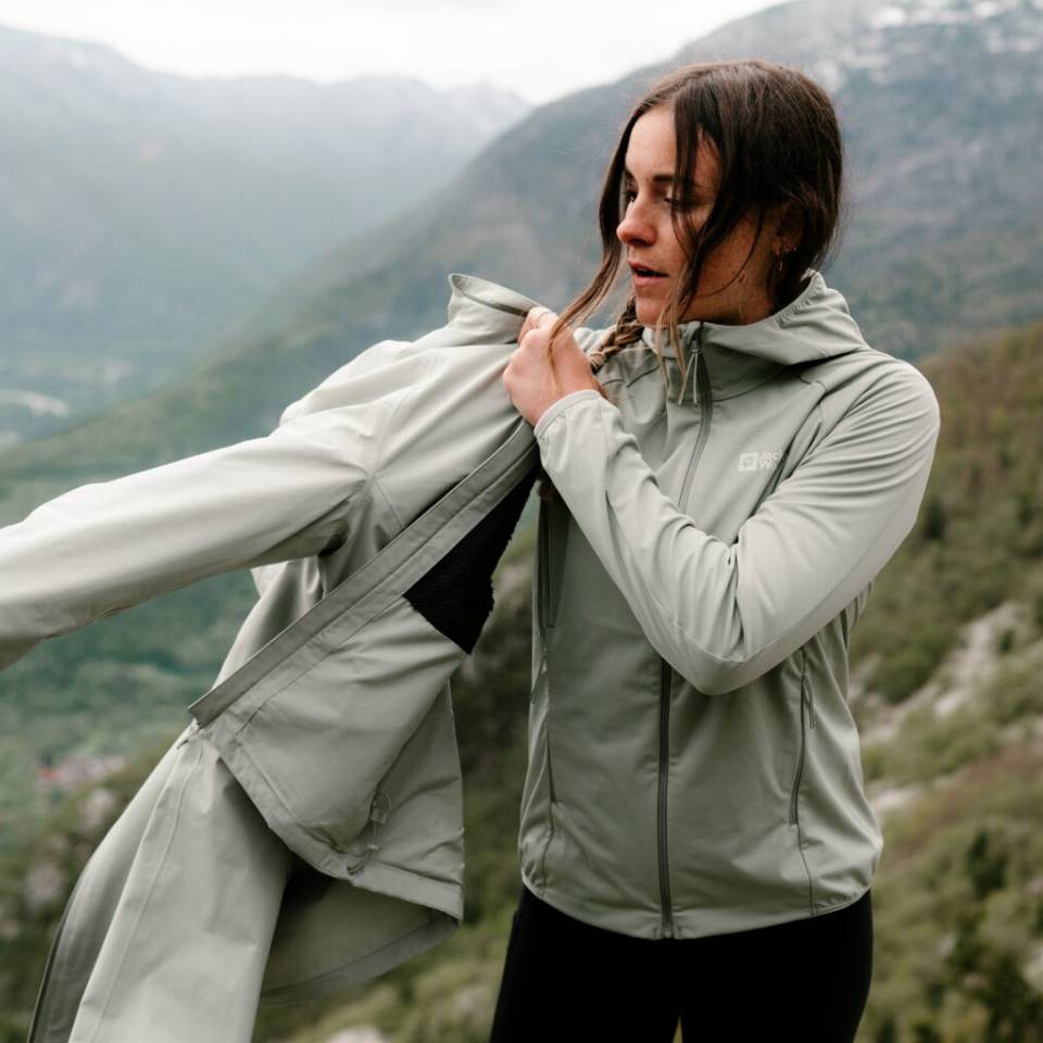 Une randonneuse dans un paysage de montagne brumeux enfile une veste de pluie